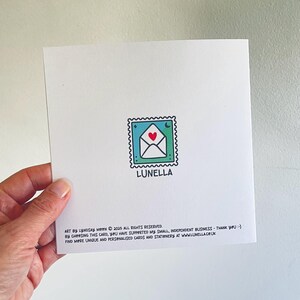 Op de afbeelding: Een witte kaart met een groene en blauwe stempel met een witte envelop met een rood hart. De tekst "LUNELLA" staat onder de stempel. De tekst "ART BY LYNDSAY MOON &copy; 2025 ALL RIGHTS RESERVED. BY CHOOSING THIS CARD, YOU HAVE SUPPORTED MY SMALL, INDEPENDENT BUSINESS - THANK YOU :-) FIND MORE UNIQUE AND PERSONALISED CARDS AND STATIONERY AT WWW.LUNELLA.CO.UK" staat onderaan de kaart.