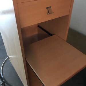 May include: A light wood mobile desk with a drawer and a pull-out shelf. The desk has a silver metal base with wheels.