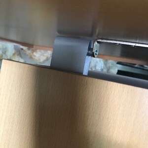 May include: Close-up of a gray metal hinge attached to a light brown wooden surface. The hinge has a silver screw.