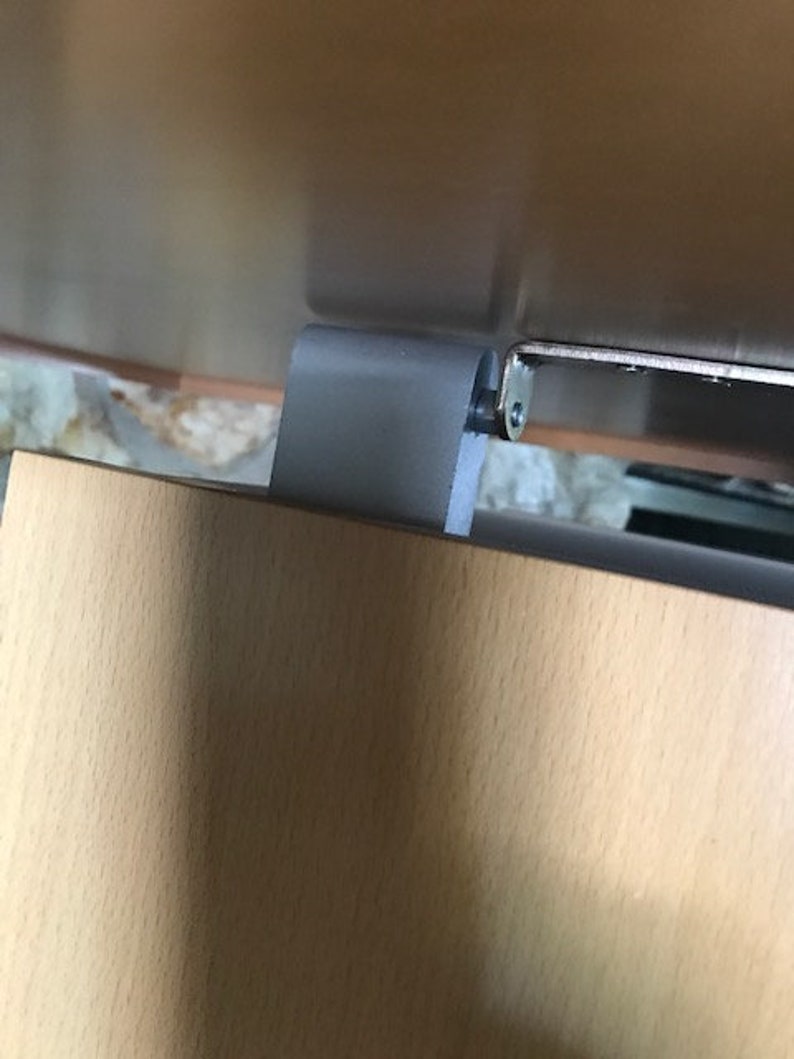 May include: Close-up of a gray metal hinge attached to a light brown wooden surface. The hinge has a silver screw.