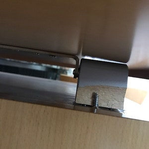 May include: Close-up of a wooden table leg with a metal bracket and a screw. The table leg is attached to the table top with a screw.
