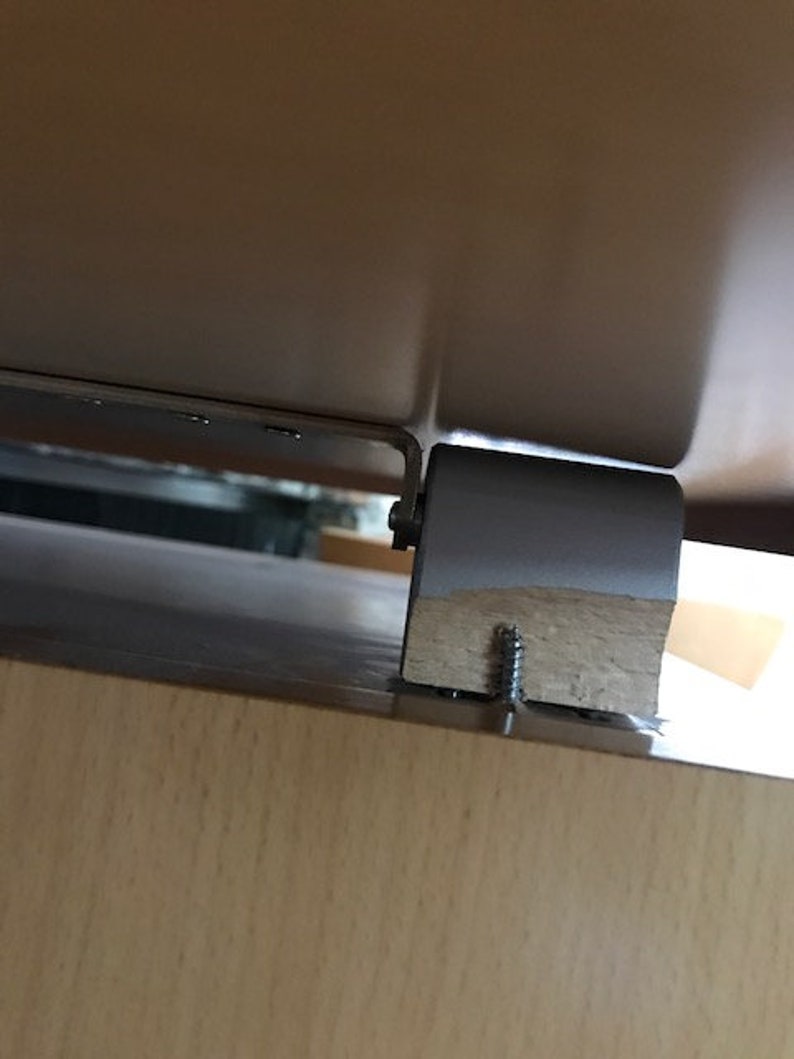 May include: Close-up of a wooden table leg with a metal bracket and a screw. The table leg is attached to the table top with a screw.