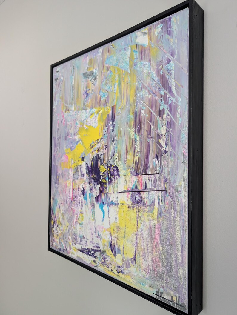May include: Abstract painting with a black frame. The artwork features a textured surface with a blend of colors, including yellow, purple, blue, and pink. The brushstrokes create a dynamic and expressive composition.
