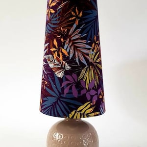 May include: A table lamp with a beige ceramic base and a conical lampshade with a tropical leaf pattern in shades of purple, blue, yellow, and orange.