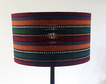 May include: A cylindrical lampshade with a colorful geometric pattern. The pattern features stripes of red, orange, green, blue, and black, with a repeating diamond design.