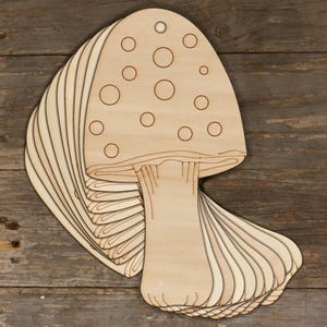 May include: A stack of unfinished wooden mushroom shapes with a hole at the top. The mushroom has a white cap with brown spots and a white stem.
