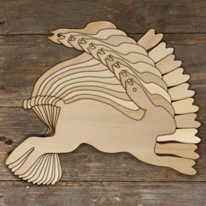 May include: A wooden hare sculpture in a running pose, crafted from layered, light-coloured wood. The design features a detailed head, flowing mane, and stylised tail and feet. The artwork is set against a rustic wooden background.