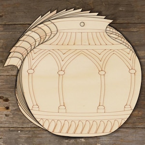 Könnte beinhalten: Ein Stapel unfertiger Holzornamente in Form einer runden Vase mit einem komplizierten Design. Die Ornamente haben oben ein Loch zum Aufhängen.