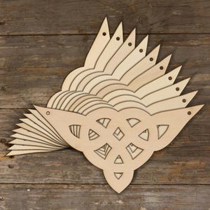 May include: A stack of multiple light-coloured wooden pennants, each featuring a triangular shape with a cutout Celtic knot design in the centre. Each individual wooden piece includes a small circular hole at the top corner for hanging purposes.