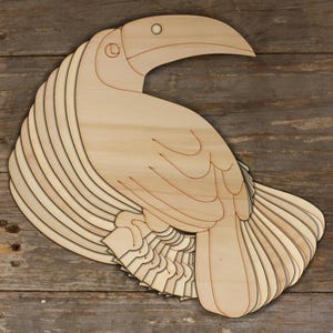 Könnte beinhalten: Ein hölzerner Tukan-Ausschnitt mit geschichteten Flügeln und einem Schnabel. Der Tukan ist aus Naturholz gefertigt und hat eine hellbraune Farbe.