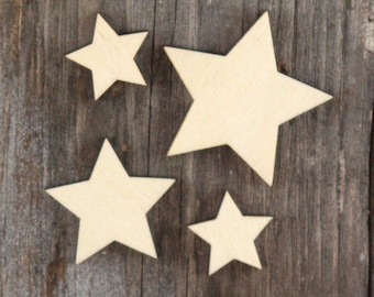 May include: Four wooden stars of varying sizes, painted white, are arranged on a brown wooden surface. The stars are all five-pointed and have a rustic, unfinished look.