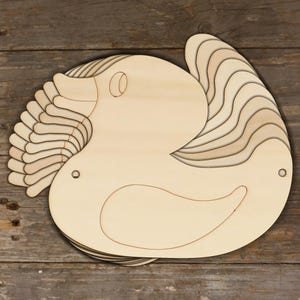May include: A stack of laser-cut wooden duck shapes, ideal for crafting. The duck has a simple, cartoonish design with a curved body, a small eye, and layered wings. The wood has a natural, light colour, and the pieces are stacked on top of each other.