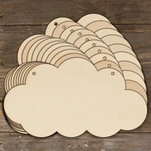 Op de afbeelding: Een stapel van 15 onafgewerkte houten wolkvormen met gaten om op te hangen. De wolken zijn in een halve cirkel gerangschikt met de grootste wolk vooraan.