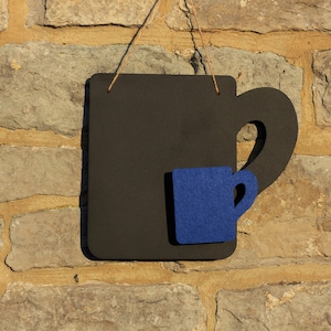May include: A black chalkboard shaped like a coffee mug with a smaller blue felt mug attached to the front.
