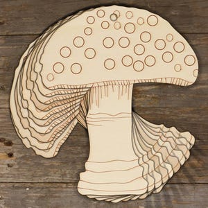 May include: A stack of wooden mushroom cutouts with a brown outline and white background. The mushroom has a rounded cap with white dots and a stem with a wavy pattern.