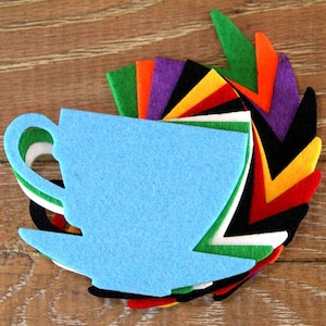 May include: A blue felt teacup and saucer cutout, layered with felt cutouts in various colours, including green, orange, red, yellow, purple, black, and white.