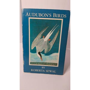 May include: A vintage book titled "Audubon's Birds" by Roberta Sewal. The cover is a deep blue with a framed illustration of a bird diving into the water. The bird is white, gray, and black with orange feet and a black beak.