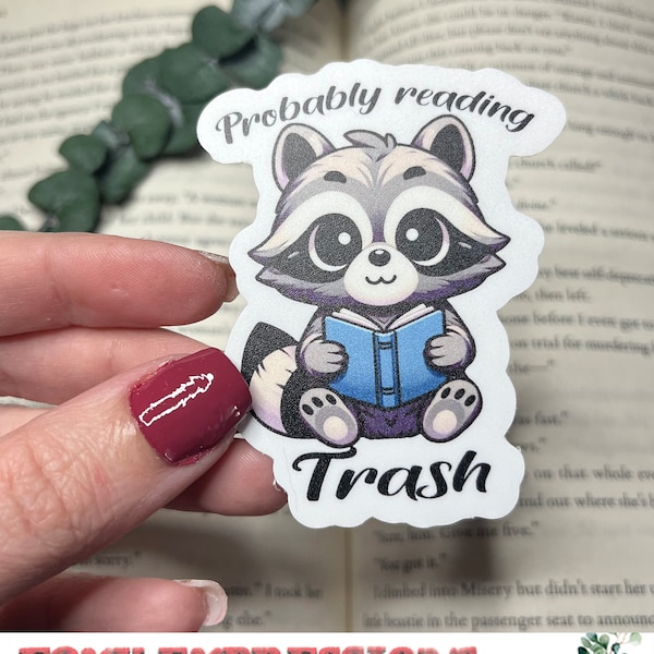 Probably reading trash, fun sticker of a trash panda reading trash. What's better? Maybe sticking this on your kindle while you read trash.