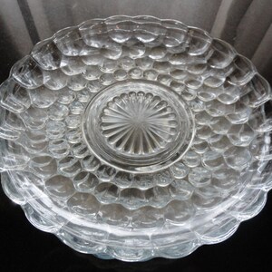 May include: A clear glass serving dish with a raised, textured design. The dish has a center section with a radiating pattern.