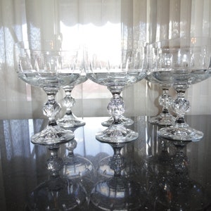 May include: Set of five clear glass champagne coupes with a cut glass design. The coupes have a round bowl and a tall stem with a decorative knob at the base.