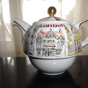 May include: White ceramic teapot with a London theme. The teapot has a gold knob and a handle. The teapot is decorated with drawings of buildings and the word "London".