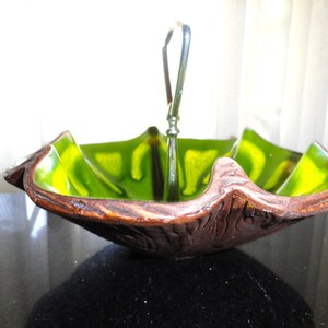 May include: A decorative serving bowl with a unique design. The bowl features a brown, textured exterior and a vibrant green and yellow interior. A silver handle rises from the center. The bowl is likely made of ceramic or a similar material.