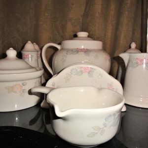 May include: A set of white ceramic kitchenware with a floral design. The set includes a creamer, sugar bowl, gravy boat, and two salt and pepper shakers.