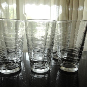 May include: Three clear glass drinking glasses with a wavy, textured design. The glasses are empty and sitting on a black surface.