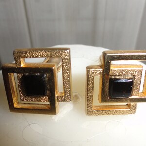 May include: A pair of gold cufflinks with black square stones set in a geometric design.