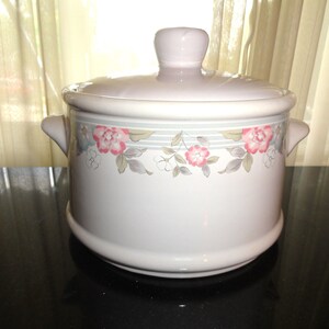 May include: White ceramic casserole dish with a lid. The dish has a floral design with pink, blue, and gray flowers. The dish has a gray and white striped band around the top.