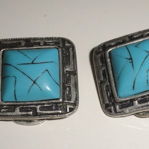 May include: A pair of silver tone clip-on earrings with turquoise blue square stones. The stones have a geometric pattern etched into them.