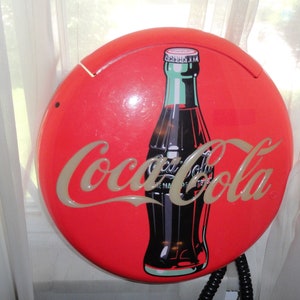 May include: A red round Coca-Cola phone with a black and green Coca-Cola bottle graphic.