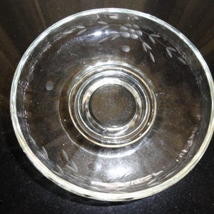 May include: Clear glass bowl with etched floral and dot designs. The bowl has a circular base with a raised center and a wide rim. The etched design includes a cluster of flowers and leaves.