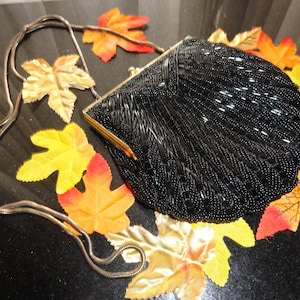 May include: A black beaded evening bag with a gold clasp and a chain strap. The bag is surrounded by fall leaves.