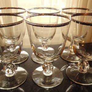 May include: Set of six clear glass goblets with a silver rim. The goblets have a round base and a stem with a knob.