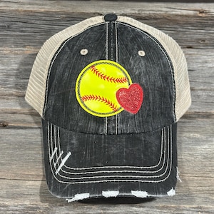Peut inclure: Casquette de camionneur noire et beige délavée. L'avant présente une balle de softball jaune avec des coutures rouges et un cœur rouge. La casquette a une visière incurvée et un dos en filet.