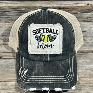 Könnte beinhalten: Schwarze und beigefarbene Trucker-Kappe mit abgenutztem Look. Die Kappe hat einen Patch auf der Vorderseite, auf dem "Softball Mom" mit einem Softball und Herzen steht.