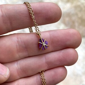 May include: A gold chain necklace with a small, raw ruby pendant. The ruby is a deep purple color and is set in a gold star-shaped frame.