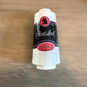 May include: A white spool of Maxi-Lock all-purpose spun polyester thread. The spool has a black and purple label with the brand name and a red logo. The thread is for serger machines.