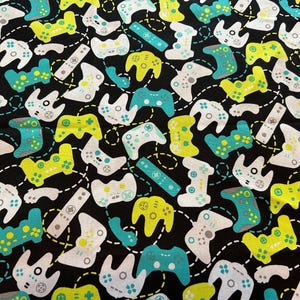 May include: Black fabric with a repeating pattern of white, yellow, and teal video game controllers. The controllers are in various positions and sizes.