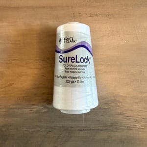 May include: A white spool of Coats & Clark SureLock thread for overlock machines. The label includes text in English, French, and Spanish. The spool contains 3000 yards of spun polyester thread.