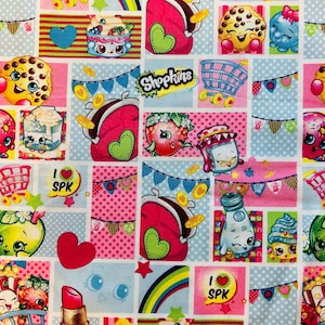 May include: A colorful fabric with a repeating pattern of cartoon characters, hearts, coins, shopping carts, and the word "Shopkins".