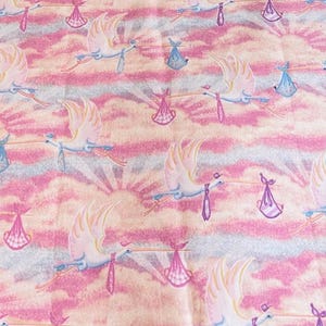 May include: A pink and blue baby shower wrapping paper with a repeating pattern of white storks carrying pink and blue packages.