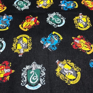 May include: Black fabric featuring repeating crests from a fantasy series. The crests are in various colors, including red, yellow, green, and blue, with detailed illustrations of animals and symbols. The crests are framed with gold borders.