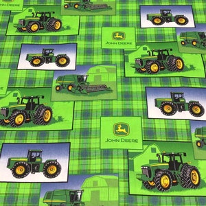 May include: Fabric with a green plaid pattern featuring illustrations of John Deere tractors and barns. The tractors are green and yellow, set against blue and green backgrounds. The John Deere logo is also present.