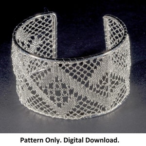 May include: A silver metal bracelet with a delicate lace pattern. The bracelet is made of wire and has a circular shape.