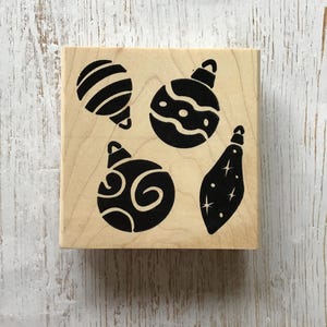 Może przedstawiać: Drewniana stempelka z czterema różnymi wzorami czarnych ozdób choinkowych. Ozdoby są stylizowane i mają różne wzory.