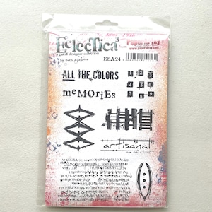 May include: A clear plastic package containing a collection of rubber stamps. The stamps feature various designs, including text that reads "ALL THE COLORS" and "memories", along with geometric shapes and numbers.
