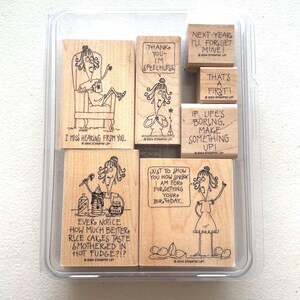 May include: A set of seven wooden rubber stamps in a clear plastic case, featuring cartoon illustrations of a woman with various humorous captions including "I miss hearing from you," "Thank you, I'm speechless," and "If life's boring, make something up!"