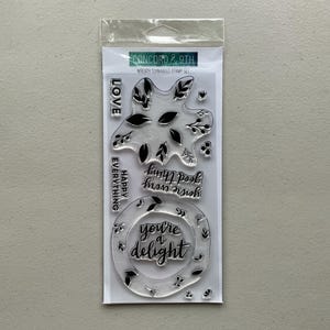 Può includere: Set di timbri trasparenti in una confezione di plastica. I timbri includono disegni floreali e frasi come "Love", "Happy Everything" e "You're a Delight". Il marchio "Concord & 9th" è stampato in alto.